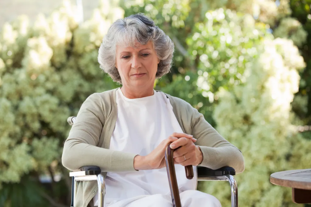 Foto de una mujer mayor sentada en una silla de ruedas y con un bastón en la mano