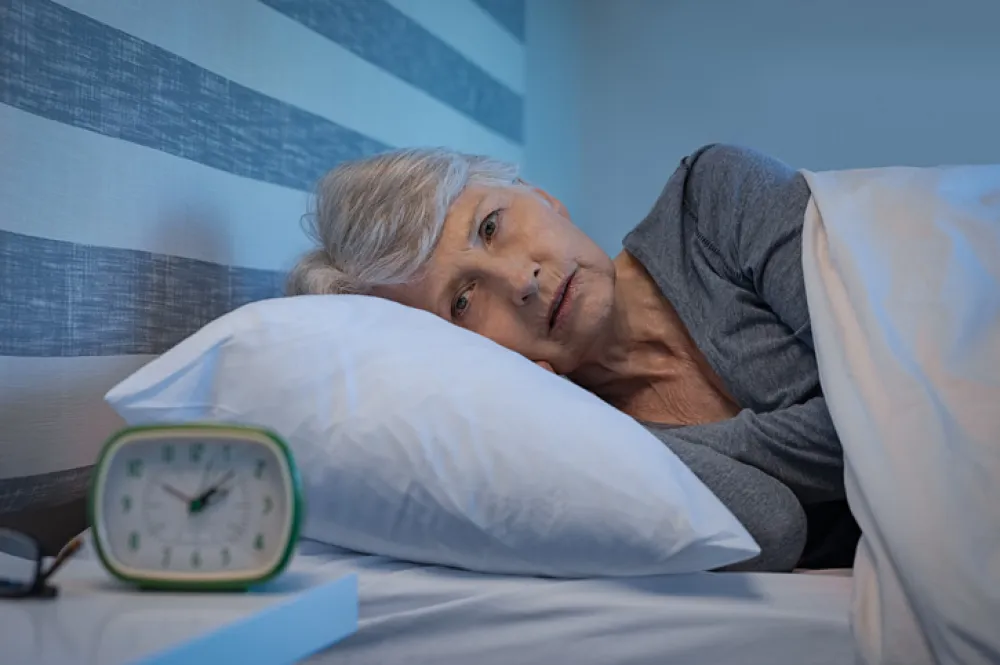 Foto de una mujer adulta tumbada en la cama despierta mirando el despertador