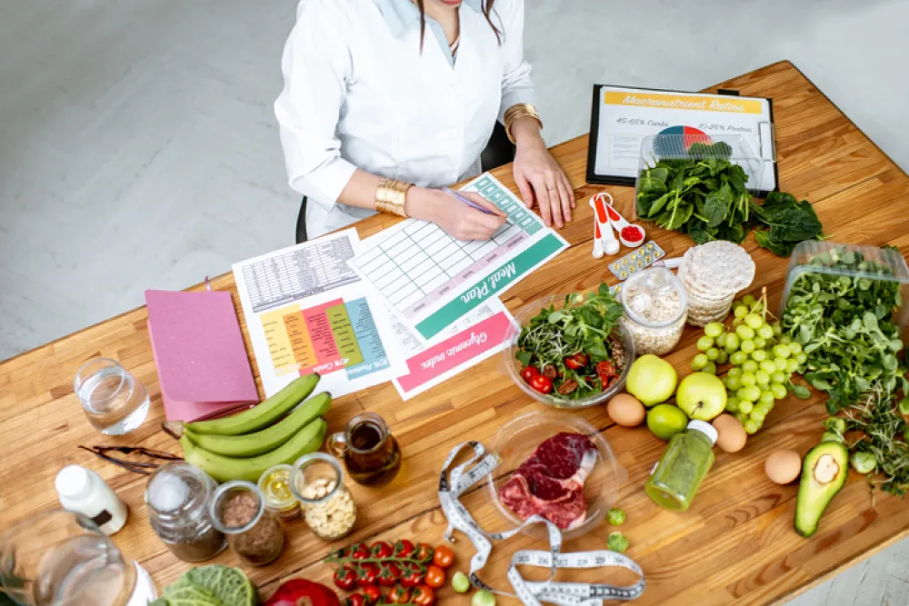 Foto desde arriba de una mesa con comida sana variada y una cocinera preparandola