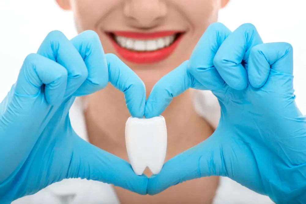 Foto de una boca sonriente y unas manos que hacen forma de corazon mientras sostienen un diente de muestra