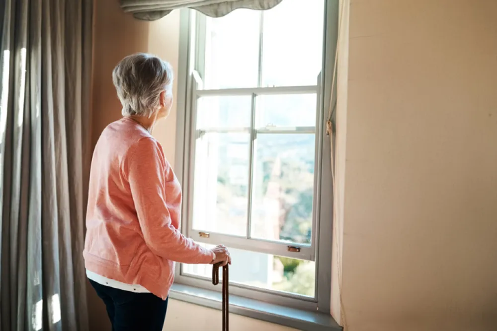 Foto de una mujer mayor mirando fuera de la ventana de su casa