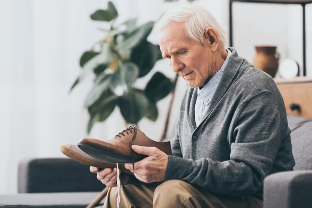 Foto de un señor mayor solo sentado mirando unos zapatos