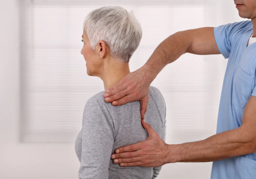 Foto de una mujer adulta sentada de espaldas y recibiendo un masaje muscular por un terapeuta