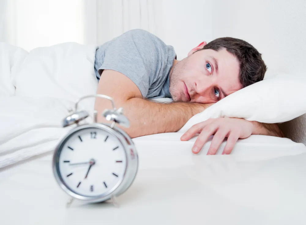 Foto hombre tumbado en una cama con los ojos abiertos y un despertador