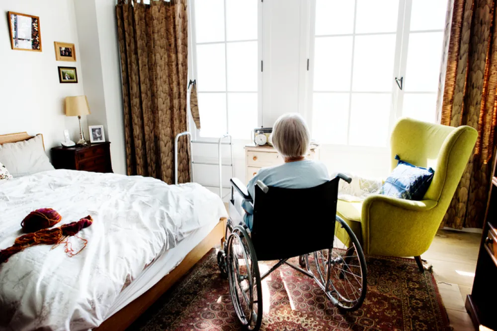 Foto de mujer de espaldas sentada en silla de ruedas en un dormitorio