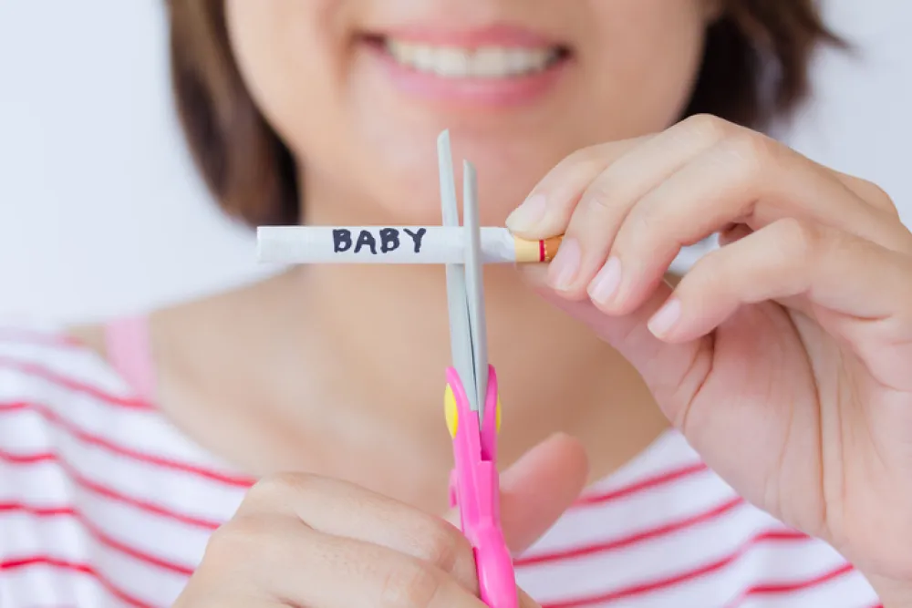 Foto de mujer cortando con tijeras un cigarrillo que tiene escrito bebé