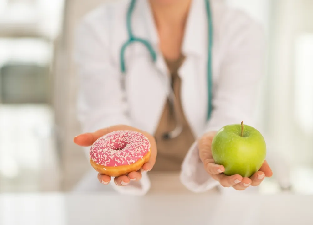 Foto de un médico que sostiene en una mano una manzana y en otra un dulce