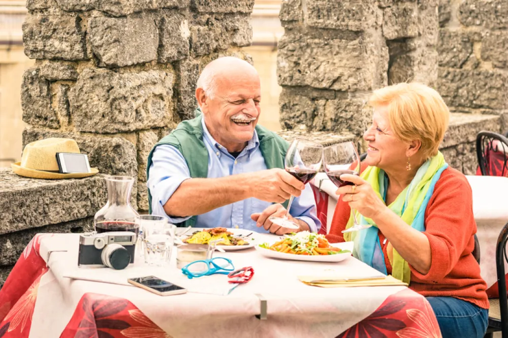 Foto pareja personas mayores sentados en una mesa comiendo y brindando