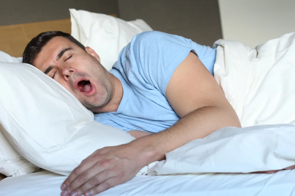 Foto de un hombre tumbado en la cama que bosteza porque no puede dormir