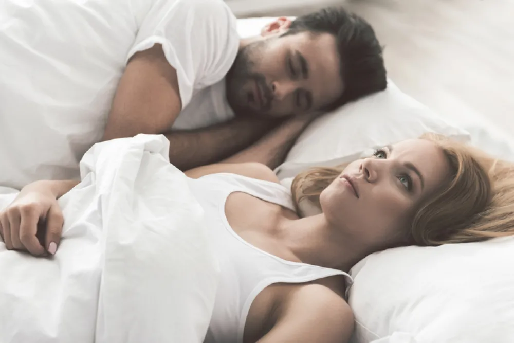Foto de una pareja tumbada en la cama y la mujer con los ojos abiertos sin poder dormir