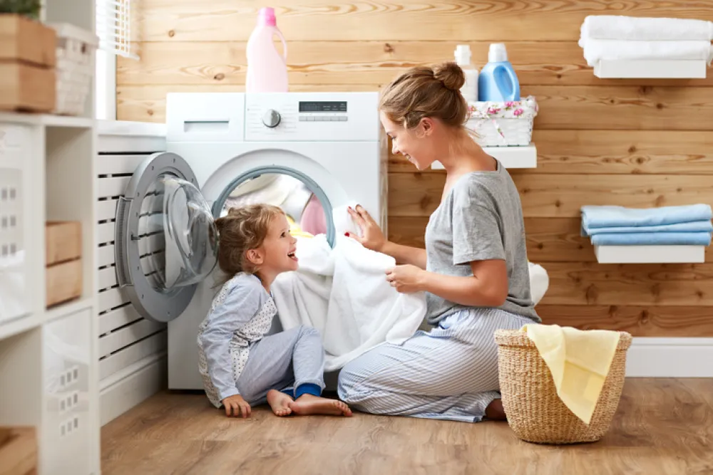 Foto madre e hija pequeña se miran sonriendo sentadas delante de la lavadora