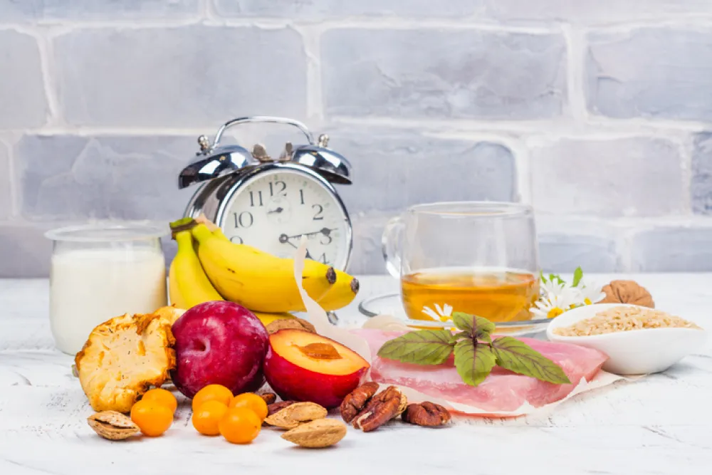 Foto de un selección de alimentos saludables acompañados por un reloj despertador antiguo
