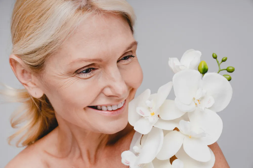Foto de una mujer adulta sonriendo mientras sostiene unas flores blancas